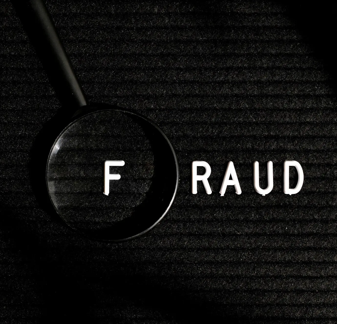 Das Wort „Fraud“ mit einem Buchstaben in einer Lupe, Draufsicht.